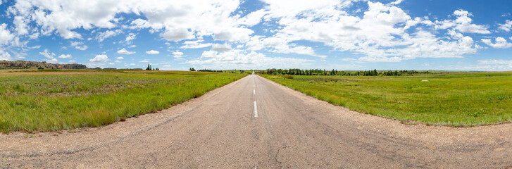 A straight asphalt road with meadows on both sides