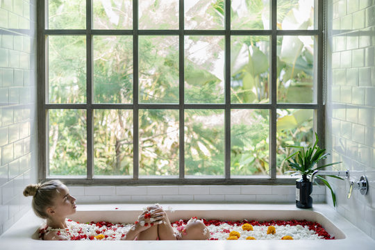 Young adult female relaxing in bath with tropical flowers