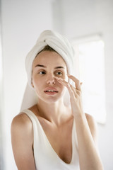 Young adult female standing in white bathroom with towel on head