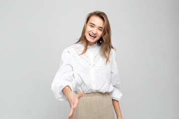 Very emotional woman laughs while tearing her stomach and holds her hands covering her face. Portrait of a beautiful woman on a white-gray background