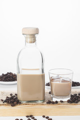 Bottle and glass of Cream coffee liqueur with ice, and coffee  beans on white rustic background.