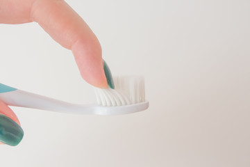  Woman finger feels soft and thin conical bristles of a toothbrush on a white background