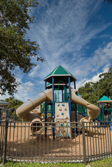 A colorful plastic playground in a park with slides behind fence