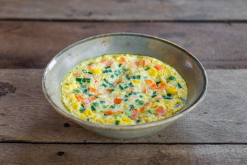 Steamed egg with vegetable in the bowl on the old wooden table.