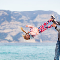 Father swinging daughter upside down, girl laughing. Family walk against the backdrop of a...