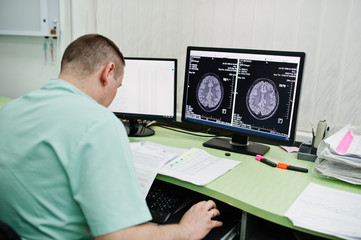 Obraz na płótnie Canvas Medical theme. Doctor in the mri office at diagnostic center in hospital, sitting near monitors of computer with human brain on it.