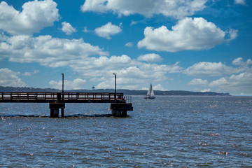 Fototapeta na wymiar A white sailboat in blue bay beyond a dark wooden pier