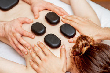 Hands of massage therapists doing back massage while hot stones on back of woman close up in spa.