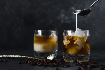 
Pouring milk into a glass of cold tasty aromatic coffee with ice on a dark background