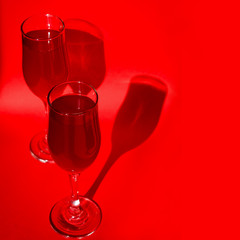 Two glasses with red wine on red background in natural sunlight with shadows