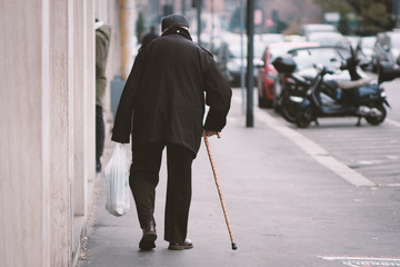 Vecchio con il bastone che cammina sul marciapiede in città a Milano