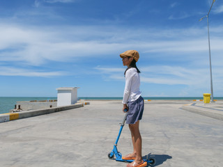 Asian girl playing stunt scooter at Hua Hin Pier in sunny day.