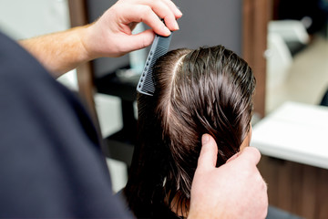 Fototapeta premium Hairdresser's hands are combing wet hair of woman in hair salon.
