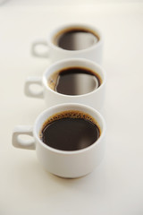 Black coffee in white cups one after another on white background