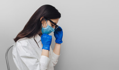 Young nurse doctor in a protective blue medical mask and gloves holding head and glasses in his hand and looking down.Physical fatigue, sleepiness.Concept of quarantine, pandemic, coronavirus COVID-19