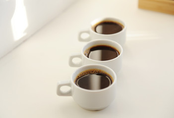 Black coffee in white cups one after another on white background