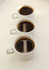Black coffee in white cups one after another on white background