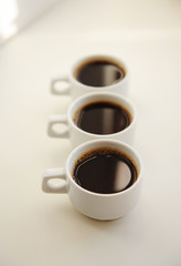 Black coffee in white cups one after another on white background