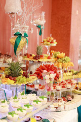 Candy bar. White wedding cake decorated by flowers standing of festive table with deserts, strawberry tartlet and cupcakes. Wedding. Reception Tartlets