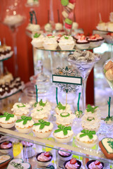 Candy bar. White wedding cake decorated by flowers standing of festive table with deserts, strawberry tartlet and cupcakes. Wedding. Reception Tartlets