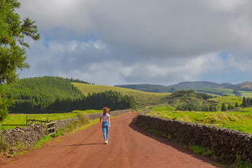 Fototapeta premium Young woman walk at country road. Fields with blue sky. Terceira