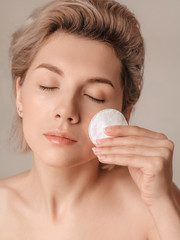 beautiful girl with blond hair cleanses the skin with a cotton pad. Shot in a studio closeup,...