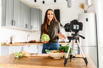 A young woman is preparing a salad in a cozy kitchen and recording of herself on camera. Food video...
