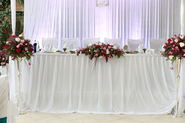 table setting at white wedding reception, floral composition, candles and cones, lights on the background