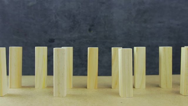 Social distance during a pandemic concept. Side view of falling wooden blocks lined up on a dark background. The principle of dominoes. Symbolic illustration of the importance of social distance