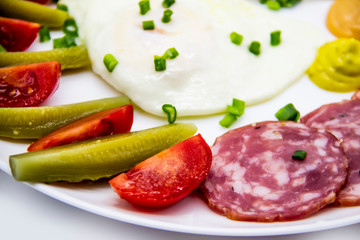 Delicious breakfast with eggs, salami, cucumbers, cherry tomatoes, sauces and green onion on top on a white plate. Healthy and tasty meal for breakfast or lunch.
