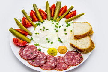 Delicious breakfast with eggs, salami, cucumbers, cherry tomatoes, slices of loaf, sauces and green onion on top on a white plate. Healthy and tasty meal for breakfast or lunch.