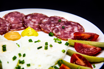 Delicious breakfast with eggs, salami, cucumbers, cherry tomatoes, sauces and green onion on top on a white plate. Healthy and tasty meal for breakfast or lunch.