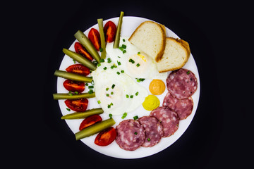 Delicious breakfast with eggs, salami, cucumbers, cherry tomatoes, slices of loaf, sauces and green onion on top on a white plate. Healthy and tasty meal for breakfast or lunch.