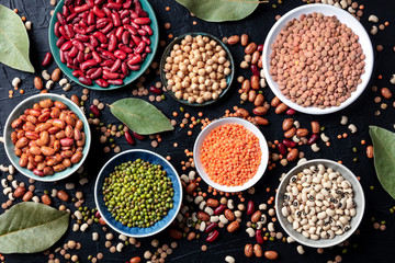 Legumes assortment, shot from the top on a black background. Lentils, soybeans, chickpeas, red...