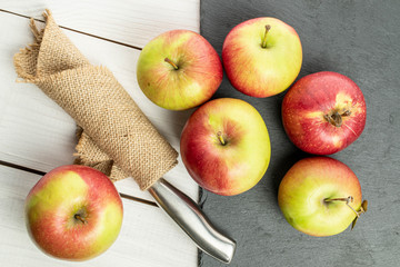 Group of six whole fresh garden apple on grey stone with knife in cloth on white wood