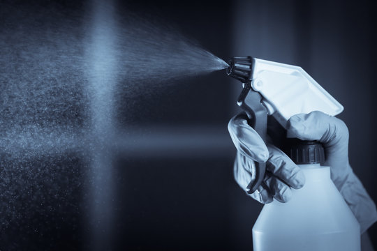 Hand with gloves holds a disinfectant dispenser and spraying
