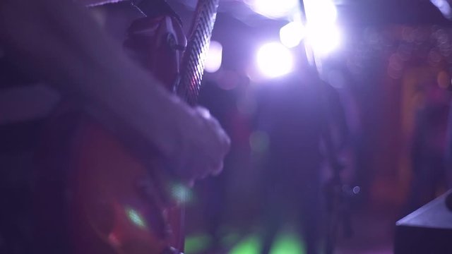 Guitarist play guitar with a pick, long fingers on fretboard under muffled lighting, close-up. A musician perform modern music on professional instrument in a crowd at a nightclub party.