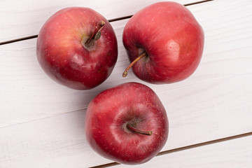Group of three whole red delicious apple on white wood
