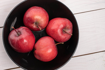 Group of four whole red delicious apple in dark bowl on white wood