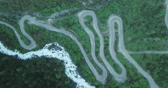 Cinematic aerial shot of white cars driving up the hill on a serpentines road next to a river in Sikkim, India.