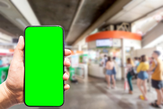 Hand holding smartphone blurred images touch of Abstract blur of people passenger stand in line queue and wait the automated entry door for the train at the sky train station blur background.