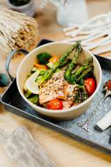 Vegetarian food rich in vitamins with salmon, asparagus, tomatoes and spices in eco box delivered by a delivery service, ordered online, decorated with raw asparagus on metal tablet