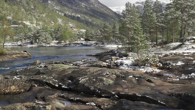 A view of the Gaula river near the Likholefossen waterfall. The river carrying its' turbulent waters to the valley. Pine forest covering mountain foothills and riverbanks.  Fresh snow is everywhere.