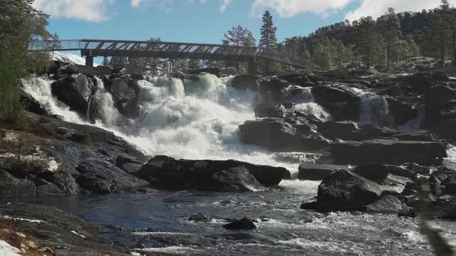 A beautiful view of the Likholefossen waterfall in Norway.  White-water gushing from under the bridge, powerful current of the mountain river. Water spray in the air. Stones are wet and glossy.