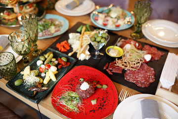 Wedding dinner table service. Wooden dishes with sliced meat and cheese with other snacks stand on a table