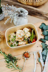 Vitamin-rich vegan food with tofu, couscous, paprika and mushrooms in eco box delivered by a delivery service, ordered online, decorated with rosemary on a wooden surface, all in a Mediterranean style