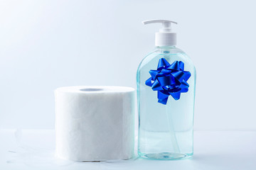 Hygienic set of toilet paper roll, bottle with antiseptic sanitizer gel with a bow as a gift (present). Hygiene products. Protection during the coronavirus epidemic. Copy space for text, close up