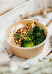 high protein food with broccholi, chicken breast, rice and aubergine in eco box delivered by a delivery service, ordered online, decorated with dried mint and spices on white wood