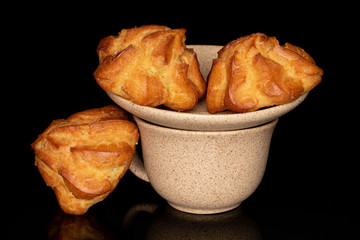 Group of three whole fresh baked profiterole with coffee cup isolated on black glass