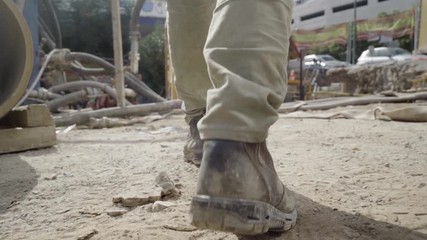Man walking through working industrial site. Follow shot to a male worker feet in boots. engineering Legs of young man stepping on stones and cables Low angle view Close up Slow motion